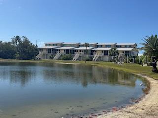A multi-unit residential building sits behind a pond under a clear blue sky — 9400 LITTLE GASPARILLA ISLAND UNIT I-9, PLACIDA, FL