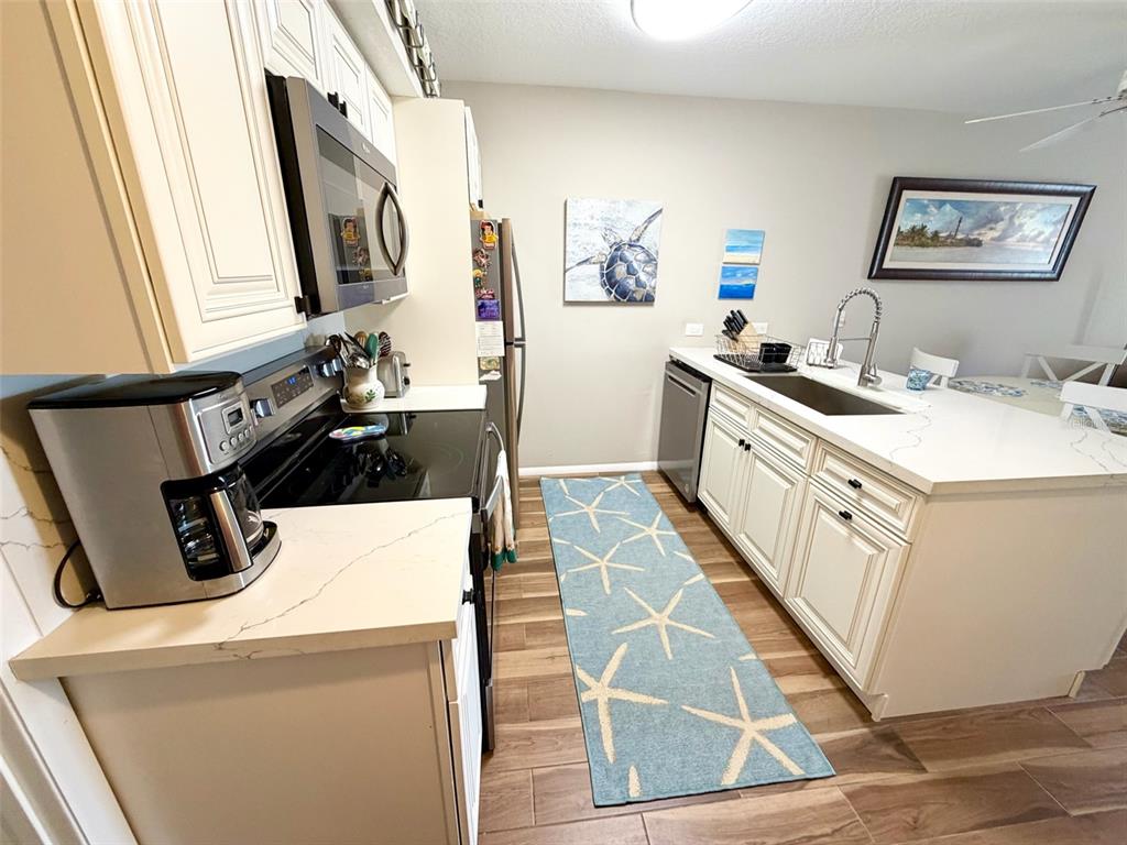 A kitchen features white cabinetry, quartz countertops, stainless steel appliances, and a starfish-patterned runner rug — 9400 LITTLE GASPARILLA ISLAND UNIT I-9, PLACIDA, FL