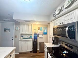 A kitchen features white cabinets, stainless steel appliances, a water cooler, and wood-look flooring — 9400 LITTLE GASPARILLA ISLAND UNIT I-9, PLACIDA, FL
