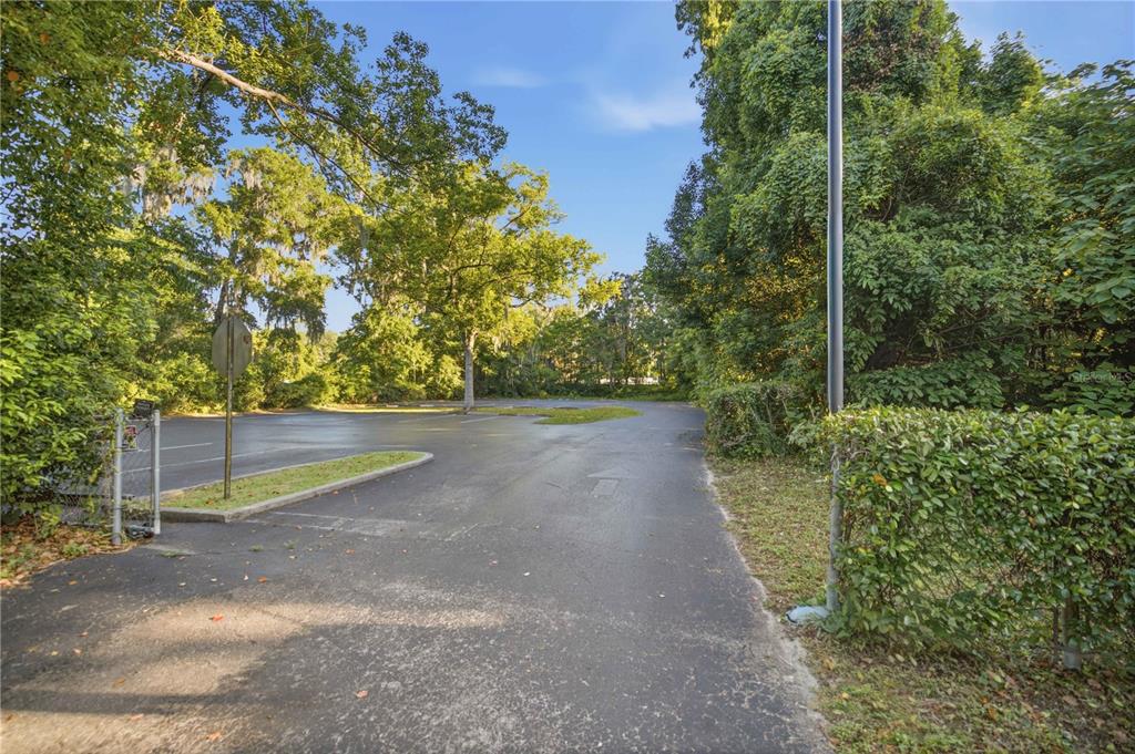 A paved parking lot is surrounded by dense green trees and a chain-link fence — TBD NE 3RD STREET, OCALA, FL