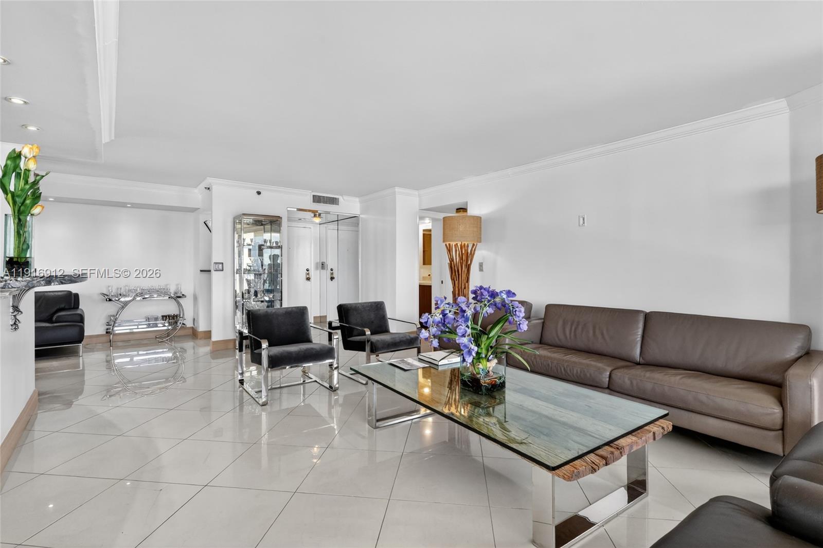 A modern living room features white tile floors, a brown leather sofa, and glass tables — 4000 Towerside Ter # 1612, Miami FL 33138, MIAMI, FL