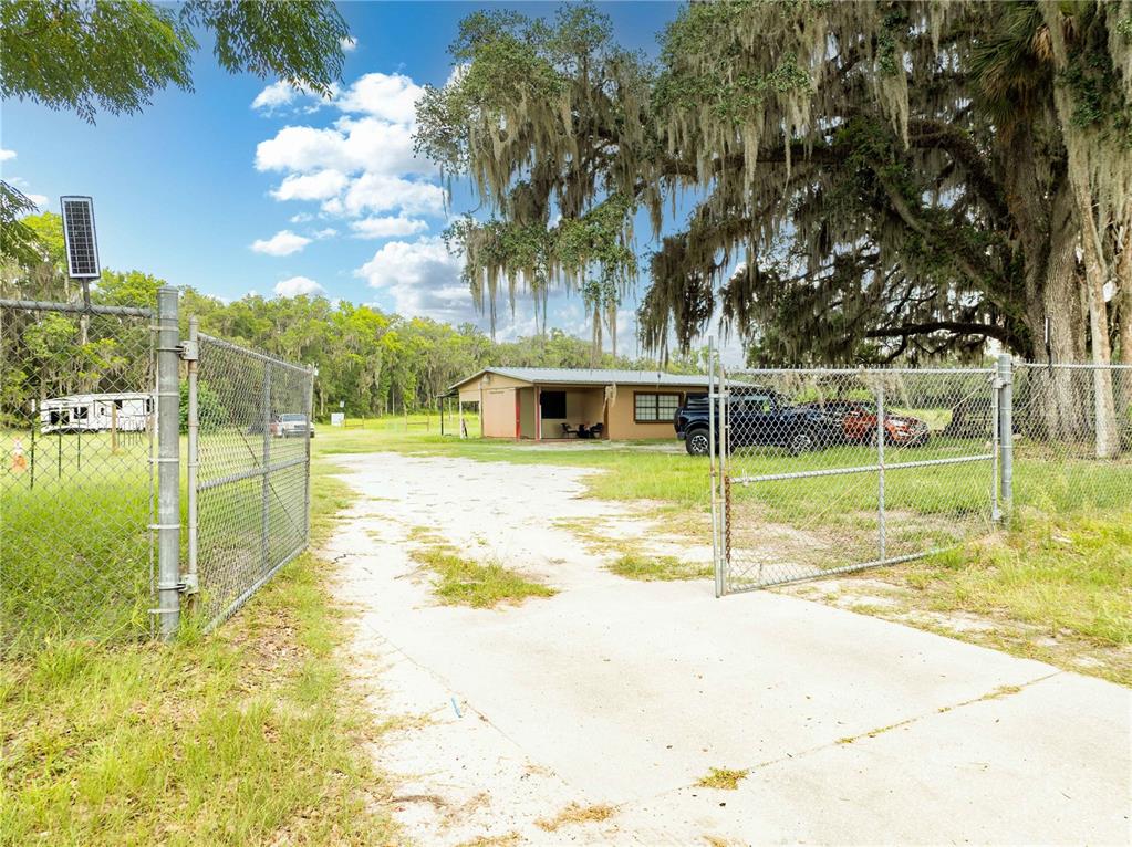 A concrete driveway leads through an open chain-link gate toward a small house — 7301 NW GAINESVILLE ROAD, OCALA, FL