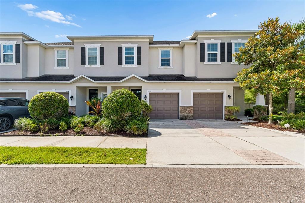 A row of two-story townhomes with attached garages and landscaped front yards under a blue sky — 606 CABERNET WAY, OLDSMAR, FL