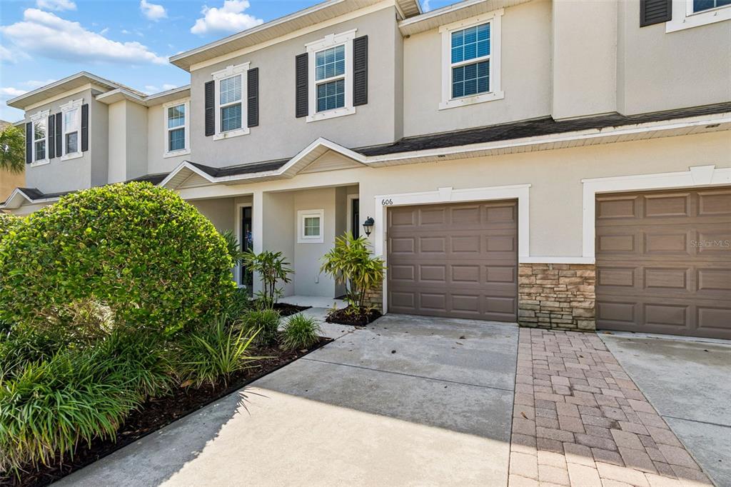 A two-story townhouse exterior features a beige facade, brown garage doors, and a paved driveway — 606 CABERNET WAY, OLDSMAR, FL
