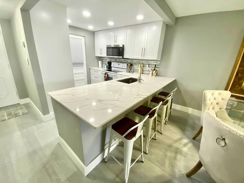 A modern kitchen features white cabinetry, a marble-patterned island with seating, and light flooring — 6461 NW 2nd Avenue # 409, Boca Raton FL 33487, BOCA RATON, FL
