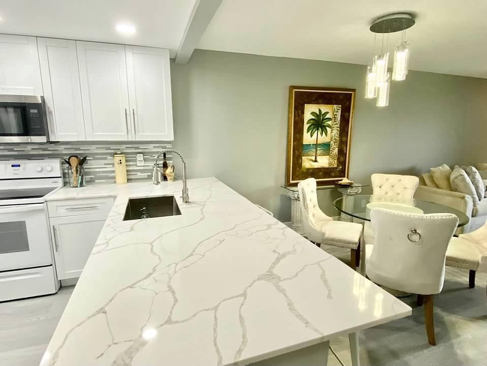 A kitchen with a white marble-patterned island, white cabinets, and an adjacent dining area — 6461 NW 2nd Avenue # 409, Boca Raton FL 33487, BOCA RATON, FL