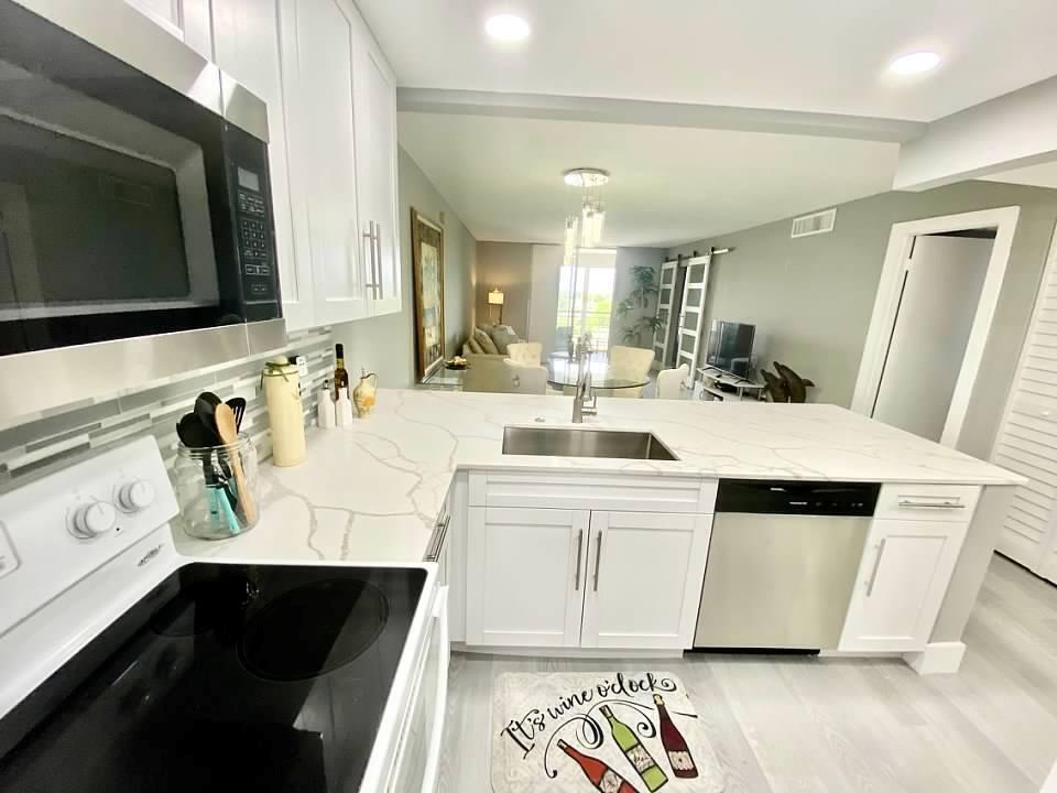 A white kitchen with quartz countertops and stainless steel appliances overlooks an open living area — 6461 NW 2nd Avenue # 409, Boca Raton FL 33487, BOCA RATON, FL