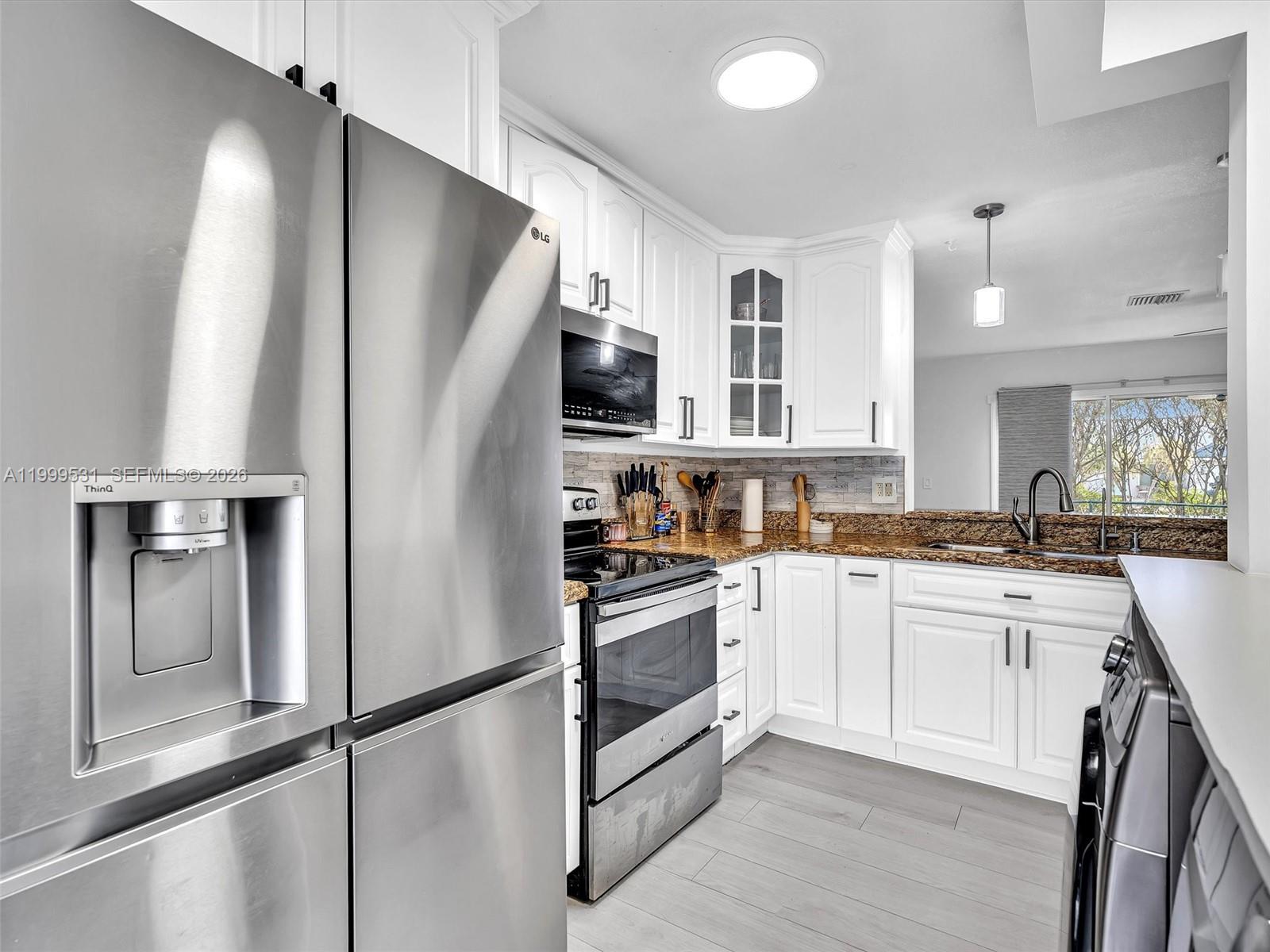 A kitchen features white cabinetry, stainless steel appliances, granite countertops, and light wood-look flooring — 3804 NW 121st Ave, Sunrise FL 33323, SUNRISE, FL