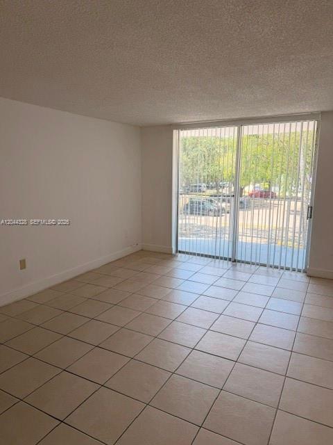 An empty room with beige tile flooring and a sliding glass door leading outside — 498 NW 165th St Rd # 204, Miami FL 33169, MIAMI, FL