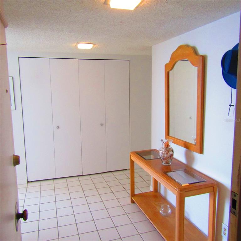 A tiled entryway features a wooden console table, a wall mirror, and white closet doors — 1430 GULF BOULEVARD UNIT 404, CLEARWATER BEACH, FL