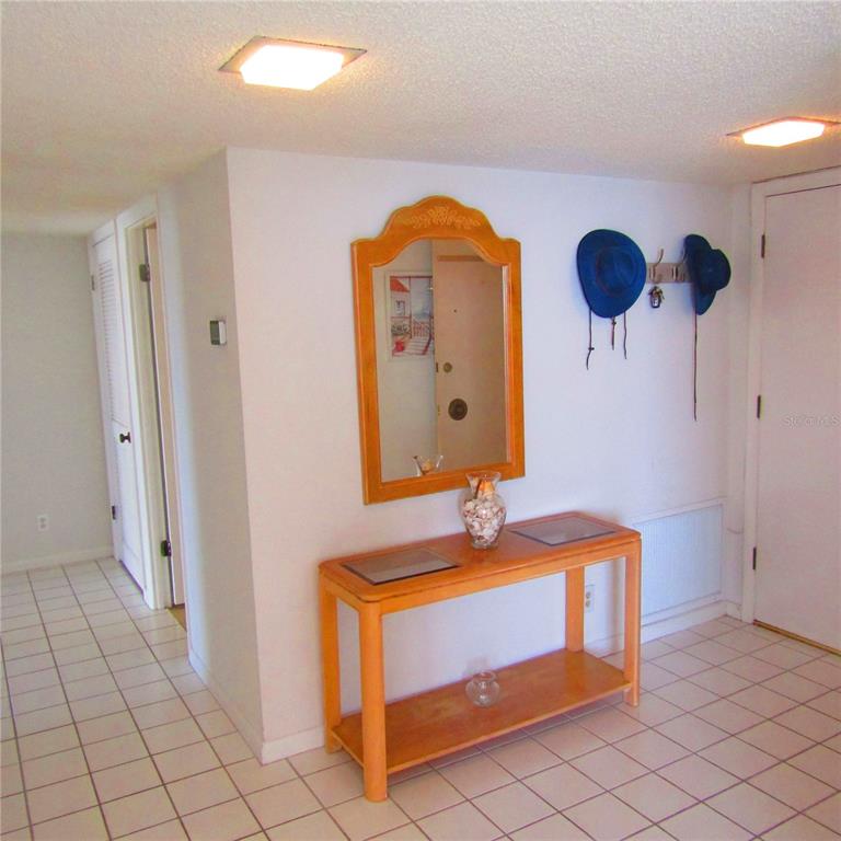 An entryway features a wooden console table, a wall mirror, and two hats on hooks — 1430 GULF BOULEVARD UNIT 404, CLEARWATER BEACH, FL