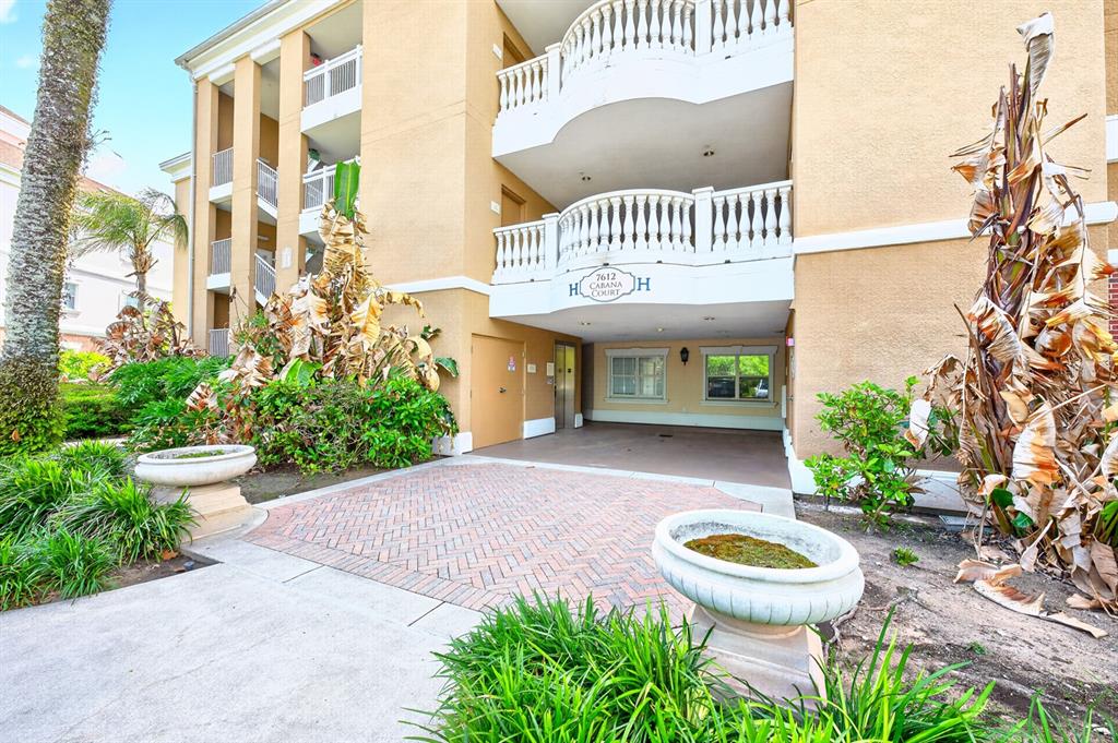 The exterior of a multi-story tan apartment building features a covered entrance and stone planters — 7612 CABANA COURT UNIT 201, REUNION, FL