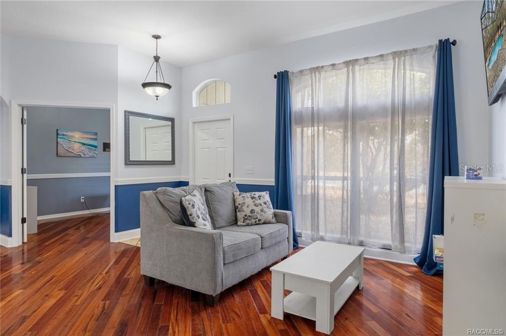A living room features a gray loveseat, white coffee table, hardwood floors, and blue curtains — 10 BOXLEAF COURT S, HOMOSASSA, FL