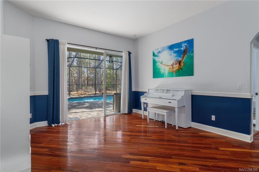 A room with hardwood floors, a white piano, and sliding doors opening to a pool — 10 BOXLEAF COURT S, HOMOSASSA, FL