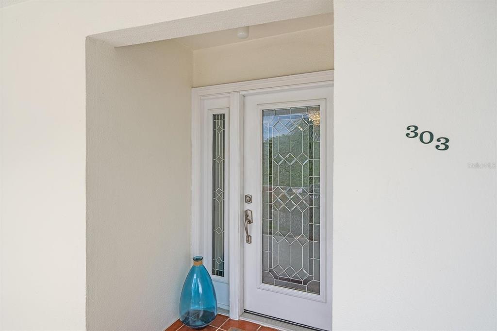A white front door with decorative glass panels and a blue vase sits under an entryway — 100 SANDS POINT ROAD UNIT 303, LONGBOAT KEY, FL