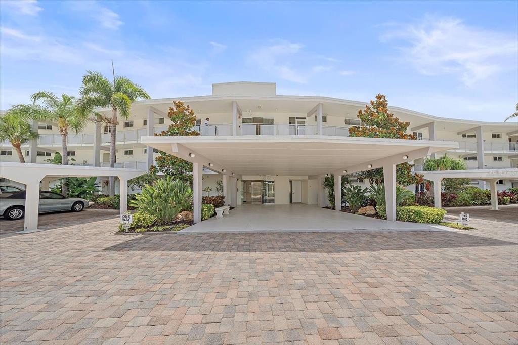 A multi-story residential building features a large covered entryway and a paved driveway — 100 SANDS POINT ROAD UNIT 303, LONGBOAT KEY, FL
