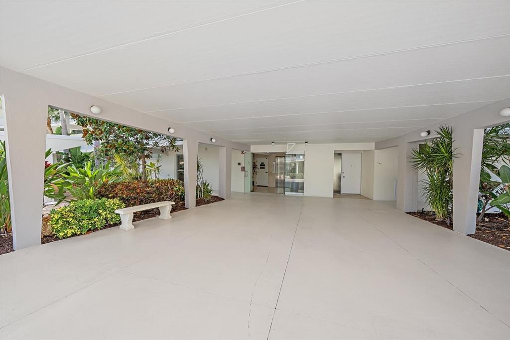 A covered outdoor entryway features a concrete floor, white pillars, and a small garden area — 100 SANDS POINT ROAD UNIT 303, LONGBOAT KEY, FL