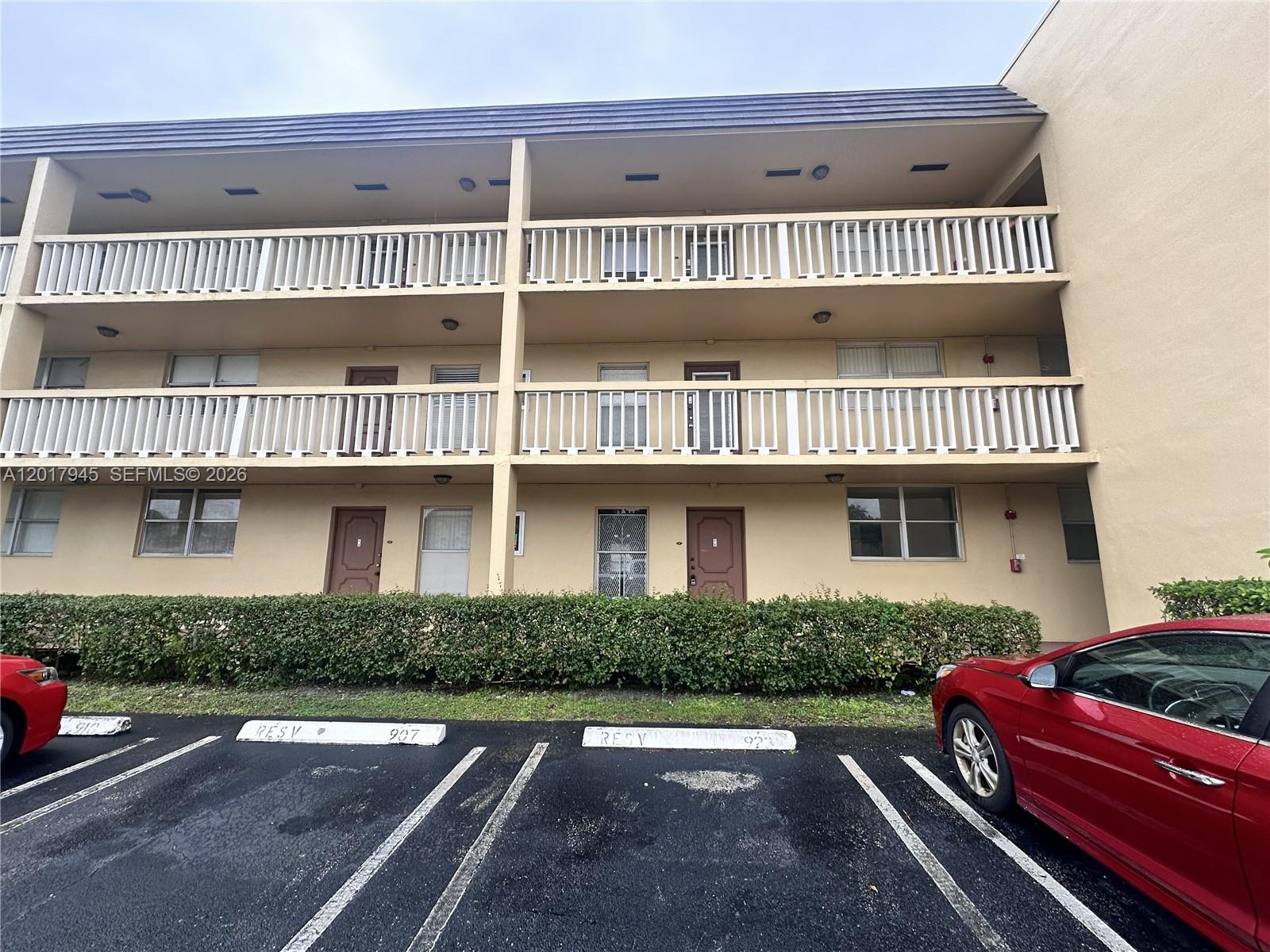 A three-story apartment building exterior features tan stucco walls, white railings, and reserved parking spaces — 6001 NW 61st Ave # 111, Tamarac FL 33319, TAMARAC, FL