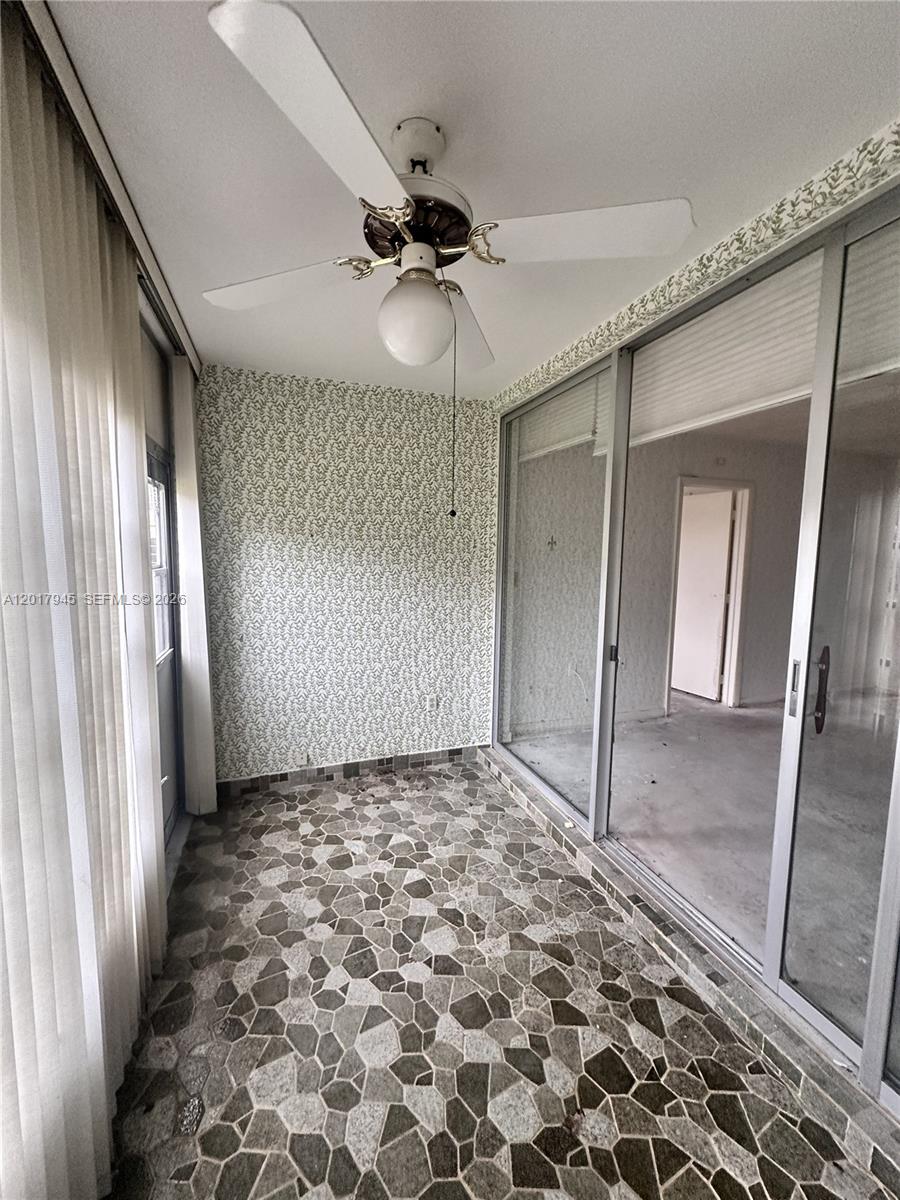 A sunroom features a patterned wallpaper wall, stone-look tile flooring, and a ceiling fan — 6001 NW 61st Ave # 111, Tamarac FL 33319, TAMARAC, FL