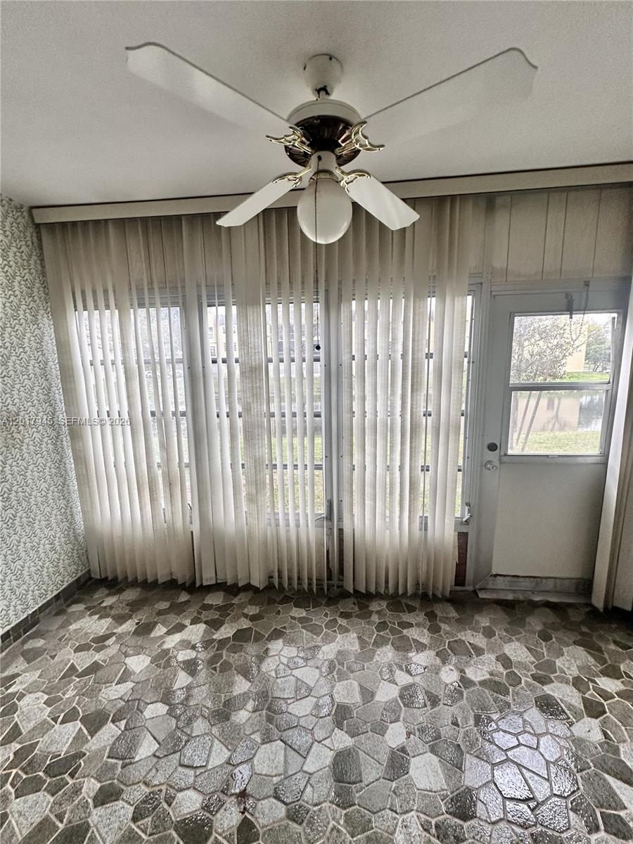 A sunroom features a stone-tiled floor, a ceiling fan, vertical blinds, and a glass door — 6001 NW 61st Ave # 111, Tamarac FL 33319, TAMARAC, FL