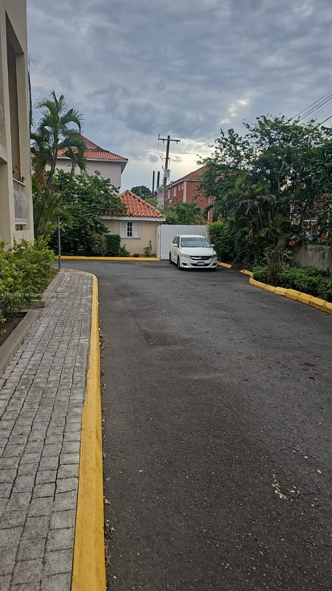 A white car is parked in a paved driveway near a building with a tiled roof — 00 Waterloo Rd, Kingston Jamaica # 01, NA, NA