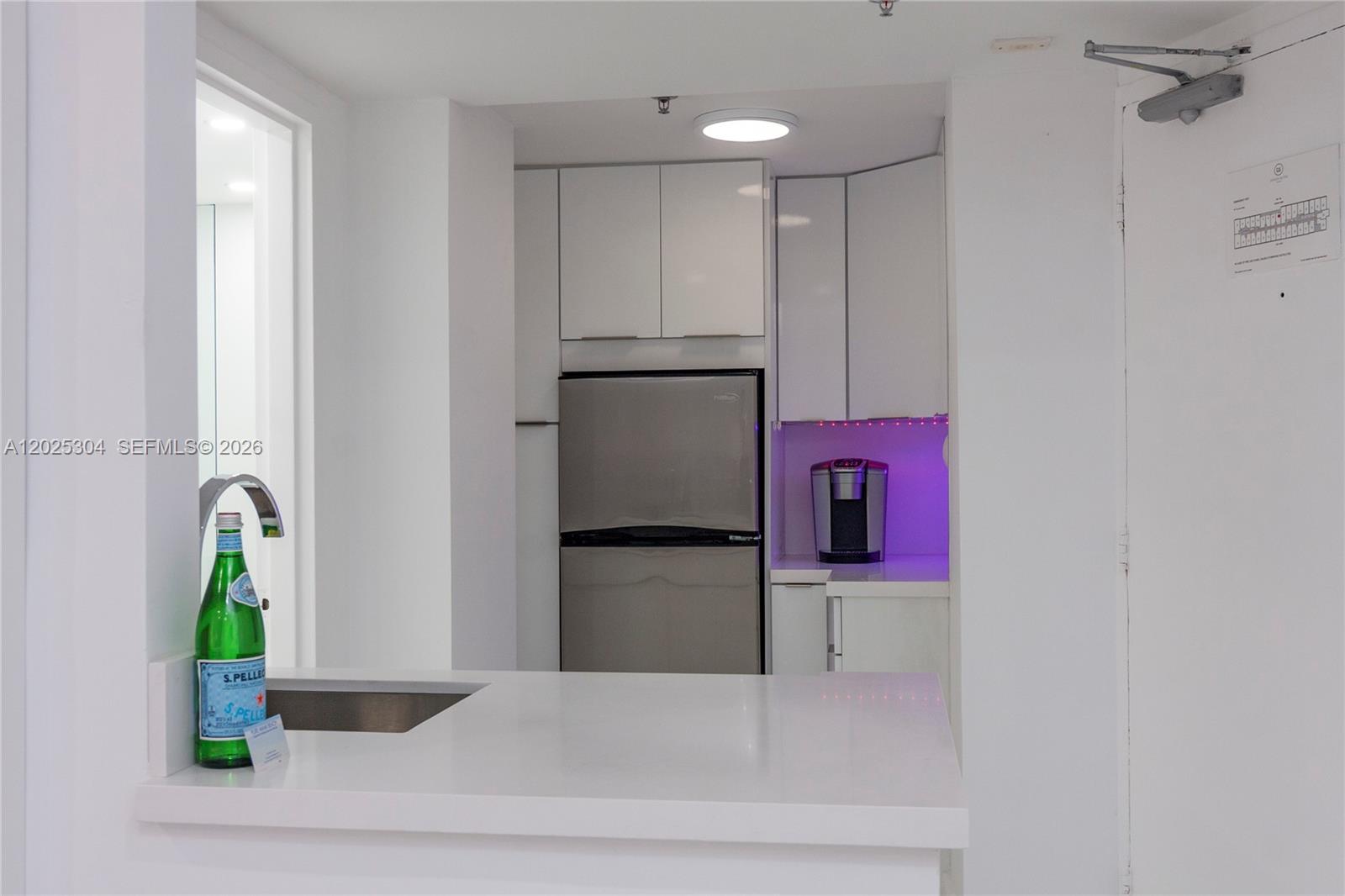 A small kitchen area features white cabinetry, a stainless steel refrigerator, and purple accent lighting — 5445 Collins Ave # 1730, Miami Beach FL 33140, MIAMI BEACH, FL