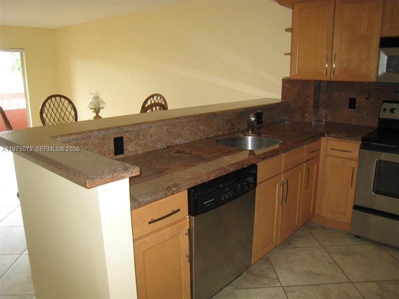 A kitchen features light wood cabinets, granite countertops, a stainless steel dishwasher, and tile flooring — 7722 Camino Real # E301, Miami FL 33143, MIAMI, FL