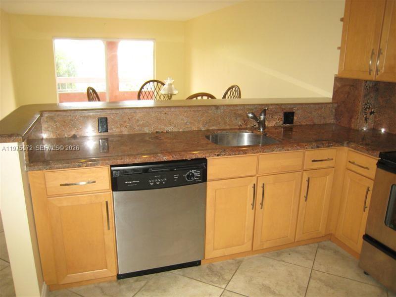 A kitchen features light wood cabinets, granite countertops, a stainless steel dishwasher, and tile flooring — 7722 Camino Real # E301, Miami FL 33143, MIAMI, FL