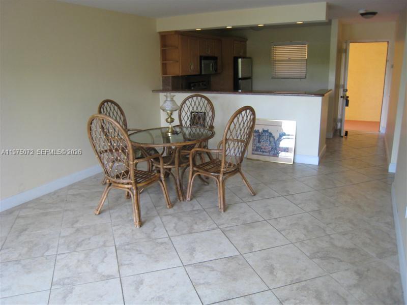 A dining area with a glass table, wicker chairs, and tile flooring near a kitchen — 7722 Camino Real # E301, Miami FL 33143, MIAMI, FL