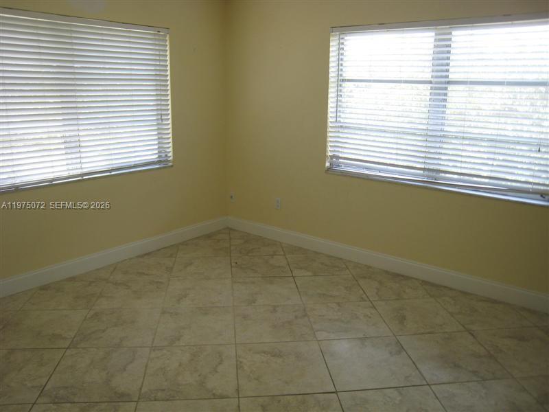 An empty room features light yellow walls, tile flooring, and two windows with white blinds — 7722 Camino Real # E301, Miami FL 33143, MIAMI, FL
