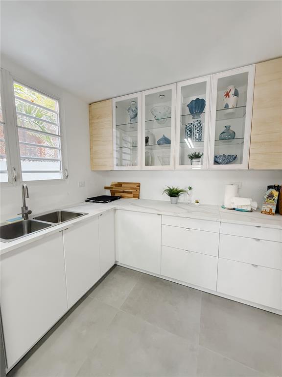 A modern kitchen features white cabinets, light wood accents, glass-front upper cabinets, and gray flooring — . ELEMI UNIT 114, GUAYNABO, PR