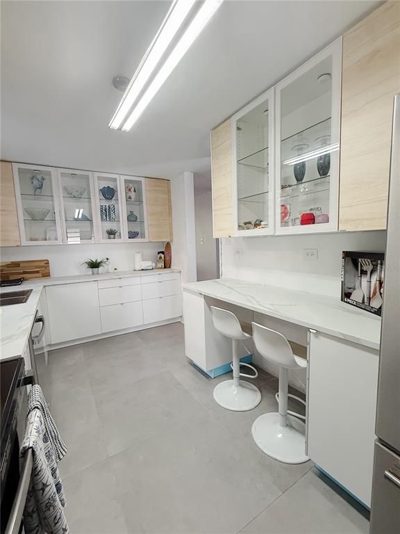 A modern kitchen features white cabinetry, a marble-look breakfast bar, and light gray tile flooring — . ELEMI UNIT 114, GUAYNABO, PR