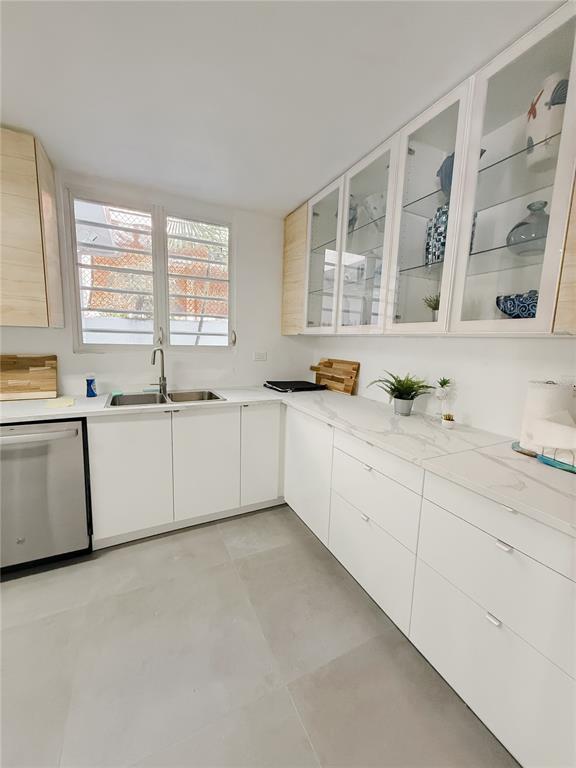 A modern kitchen features white cabinets, marble-look countertops, glass-front upper cabinets, and a stainless dishwasher — . ELEMI UNIT 114, GUAYNABO, PR