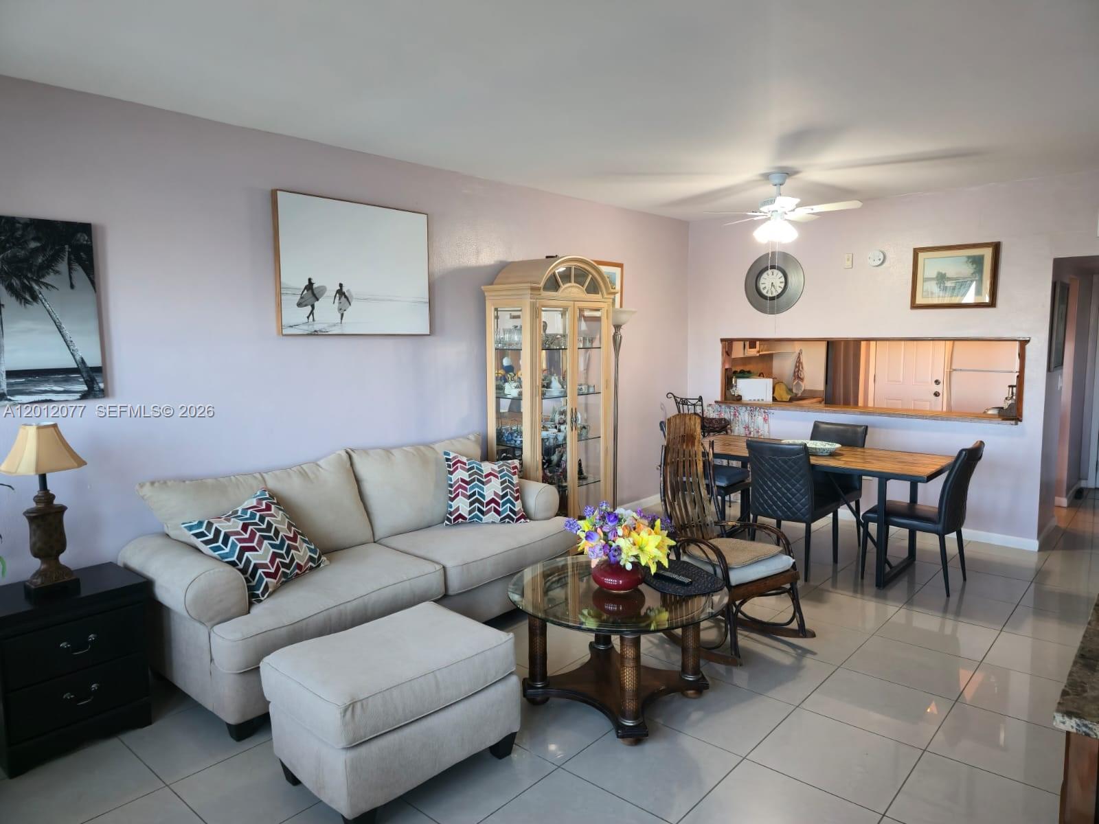 A living room with a beige sofa, glass coffee table, and dining area with tile floors — 18707 NE 14th Ave # 727, Miami FL 33179, MIAMI, FL
