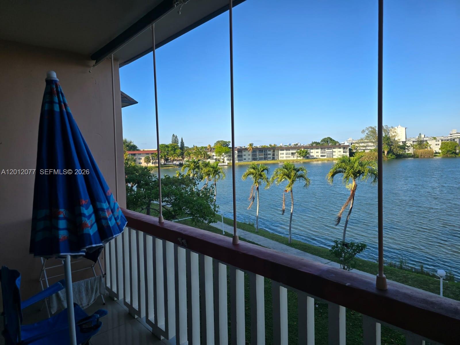 A balcony overlooks a lake with palm trees and apartment buildings in the distance — 18707 NE 14th Ave # 727, Miami FL 33179, MIAMI, FL