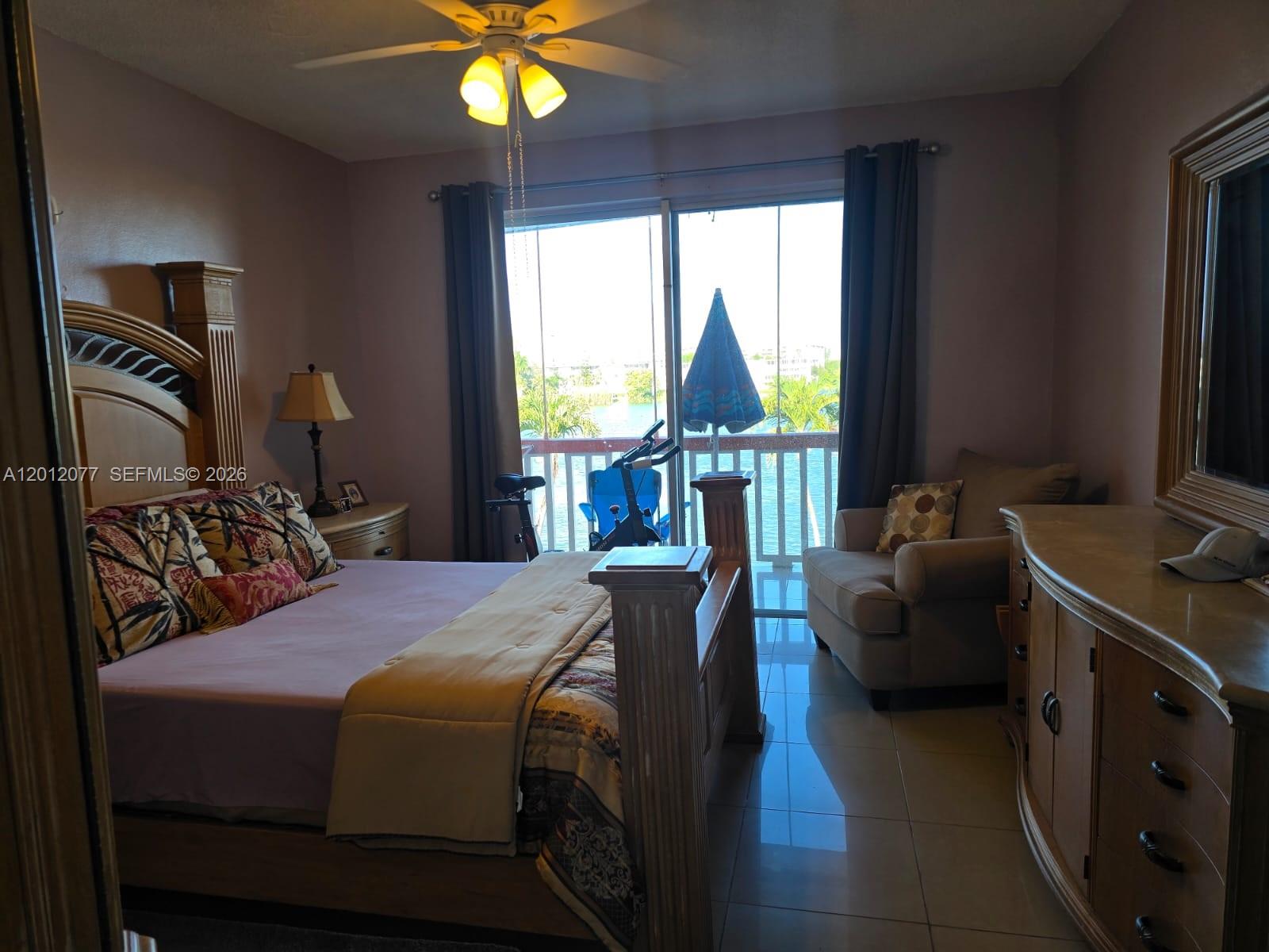 A bedroom features a wooden bed frame, tile flooring, and a balcony with water views — 18707 NE 14th Ave # 727, Miami FL 33179, MIAMI, FL