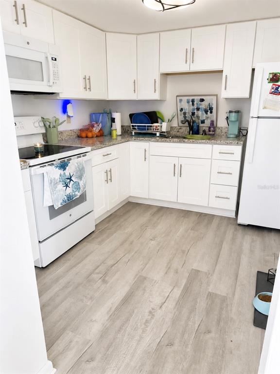 A kitchen features white cabinets, stainless steel appliances, granite countertops, and light wood-look flooring — 563 FAIRWAYS DRIVE UNIT A, OCALA, FL