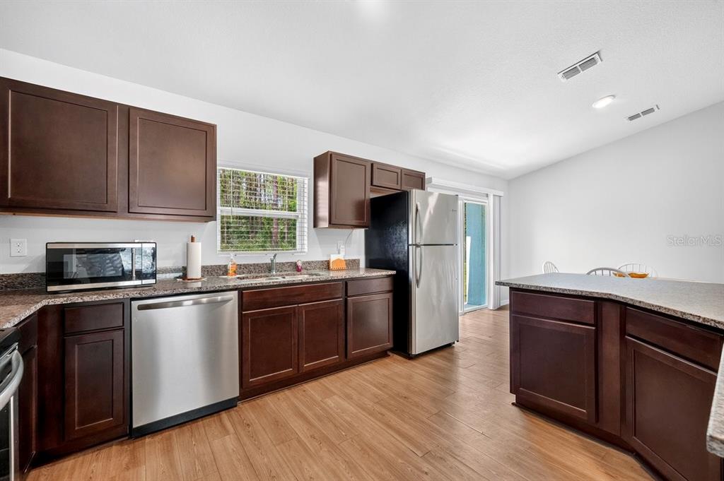 A kitchen features dark wood cabinets, granite countertops, stainless steel appliances, and wood-look flooring — 3 KARANDA COURT, PALM COAST, FL