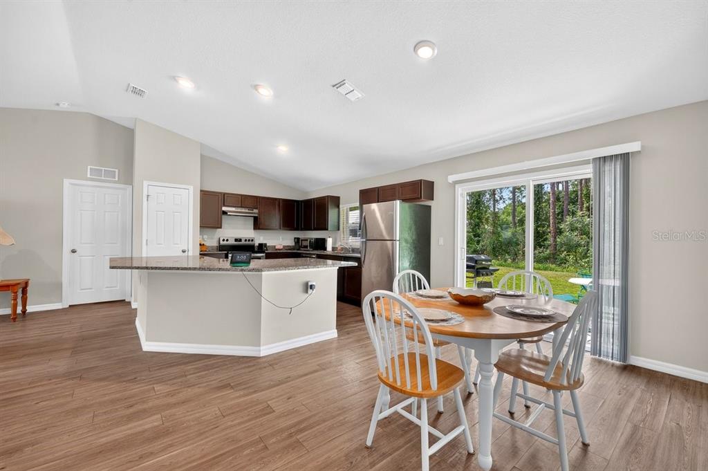 A kitchen and dining area with dark cabinets, granite countertops, and a sliding glass door — 3 KARANDA COURT, PALM COAST, FL