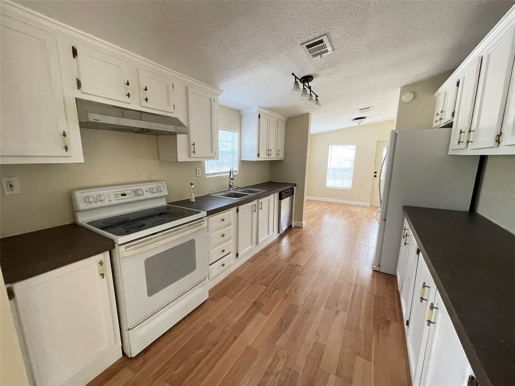 A kitchen features white cabinets, dark countertops, a white stove, and light wood-look flooring — 13716 NE COUNTY ROAD 1471, WALDO, FL