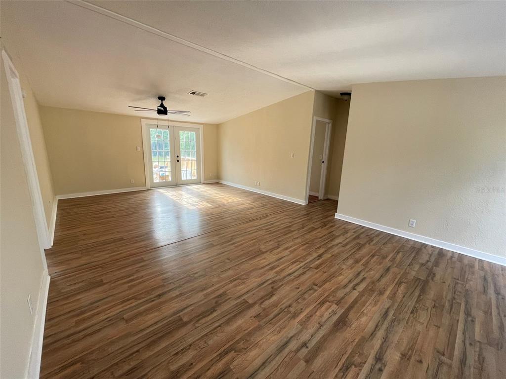 An empty living room features light-colored walls, wood-look flooring, a ceiling fan, and glass doors — 13716 NE COUNTY ROAD 1471, WALDO, FL