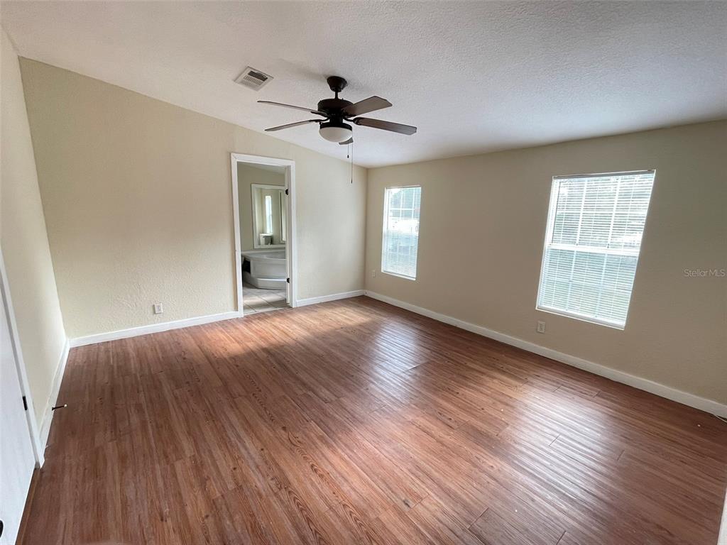 A bedroom features wood-look flooring, beige walls, a ceiling fan, and a doorway to a bathroom — 13716 NE COUNTY ROAD 1471, WALDO, FL