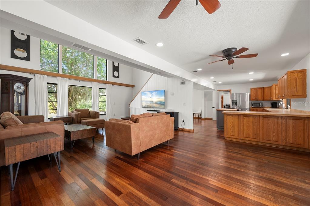 An open-concept living room and kitchen feature hardwood floors, vaulted ceilings, and large windows — 5674 BLACKJACK COURT S, PUNTA GORDA, FL