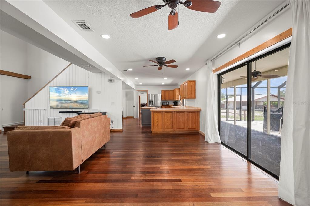 A living room with hardwood floors, a brown sofa, and an open kitchen with wood cabinets — 5674 BLACKJACK COURT S, PUNTA GORDA, FL