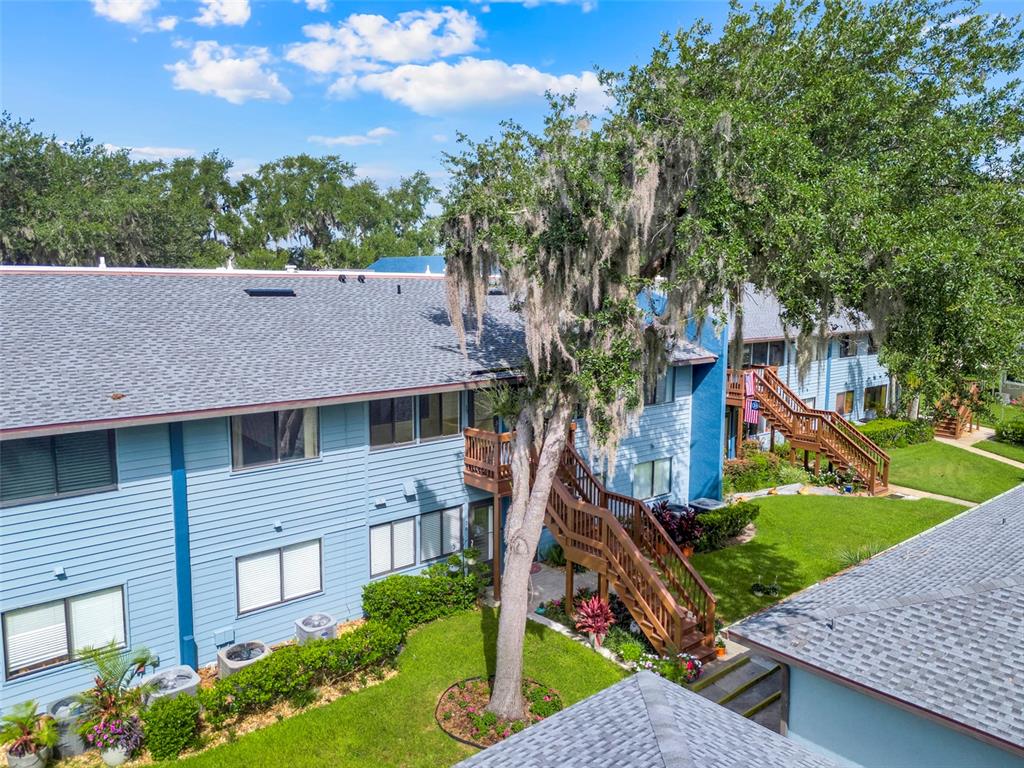 An aerial view shows a blue two-story apartment building with wooden stairs and landscaping — 608 S MAIN AVENUE UNIT 35, MINNEOLA, FL