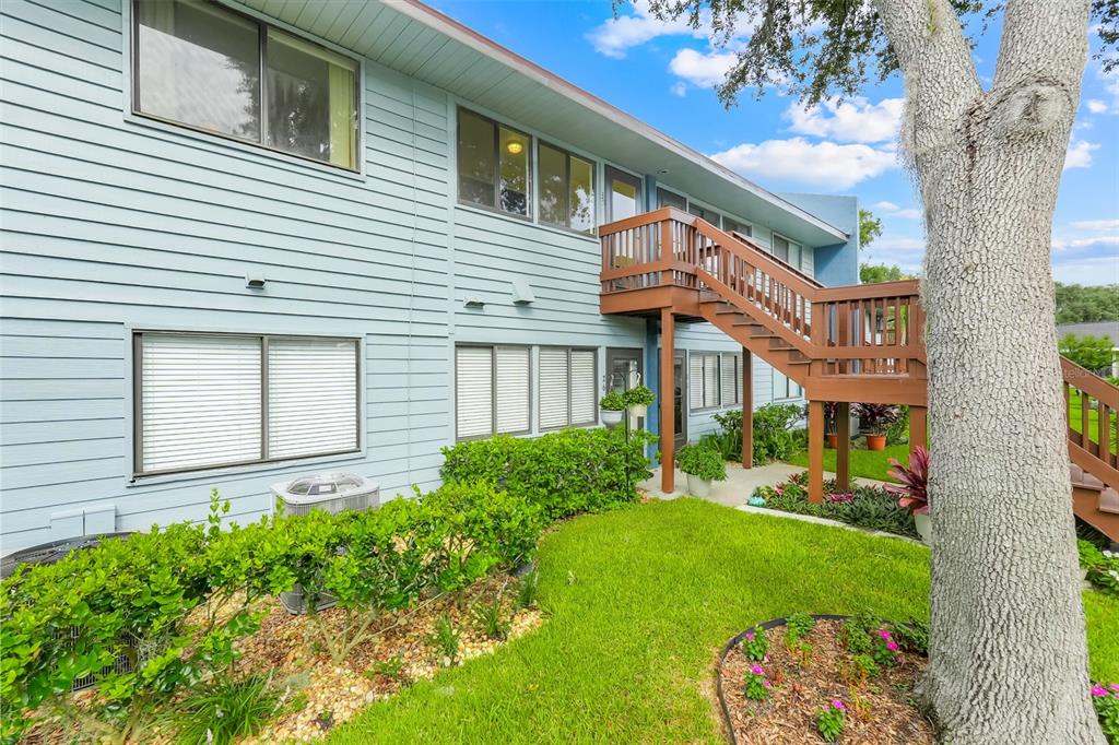 The exterior of a two-story light blue building features a wooden staircase and landscaping — 608 S MAIN AVENUE UNIT 35, MINNEOLA, FL