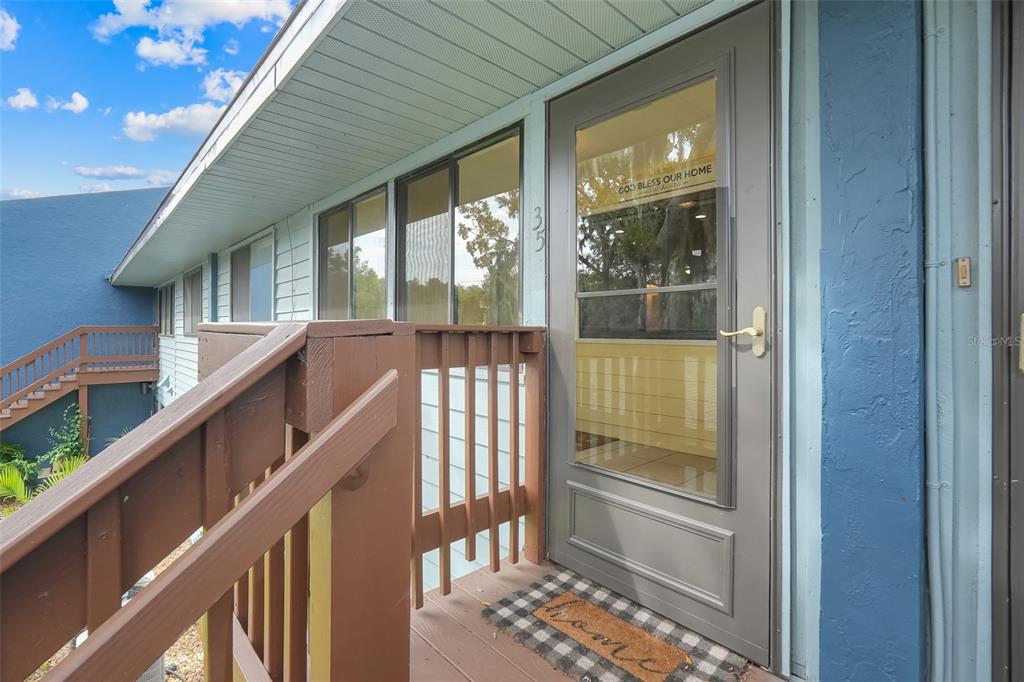 An exterior view of a home entrance with a wooden deck, railing, and storm door — 608 S MAIN AVENUE UNIT 35, MINNEOLA, FL
