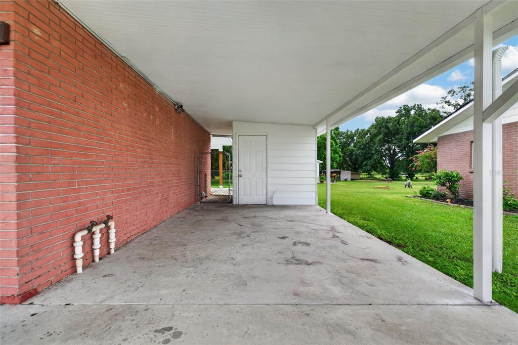A covered concrete carport features a red brick wall, a white door, and support posts — 5838 OLD BARTOW EAGLE LAKE ROAD, WINTER HAVEN, FL