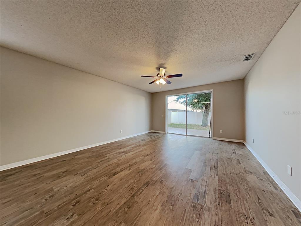 An empty living room features wood-look flooring, a ceiling fan, and sliding glass patio doors — 716 KNOLLWOOD DRIVE, DAVENPORT, FL