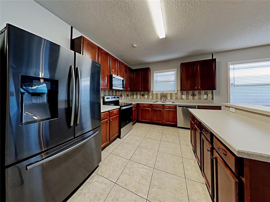A kitchen features dark wood cabinets, stainless steel appliances, tile flooring, and a breakfast bar — 716 KNOLLWOOD DRIVE, DAVENPORT, FL